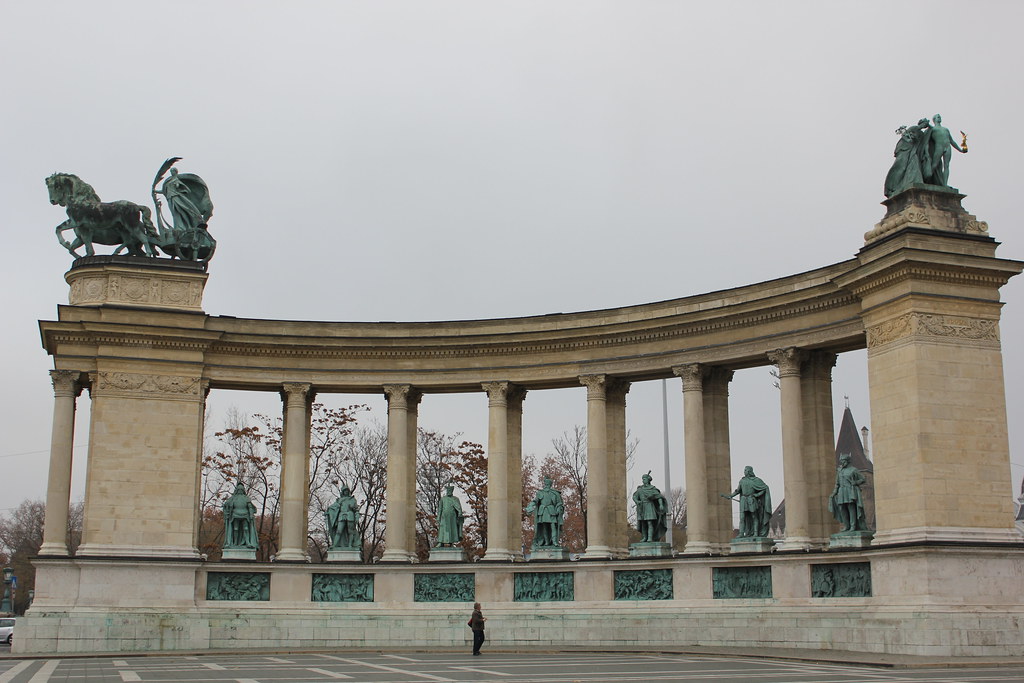 Vista frontal de la Plaza de los Héroes con estatuas en Budapest en día nublado.