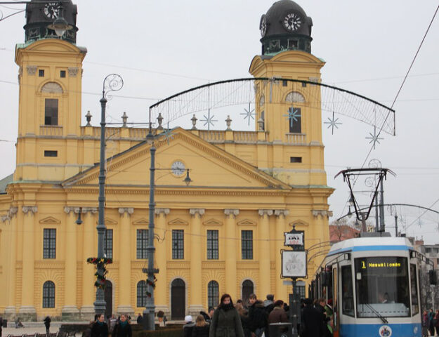 Gente caminando cerca del tranvía y la iglesia amarilla en la plaza Kossuth Lajos, Debrecen.
