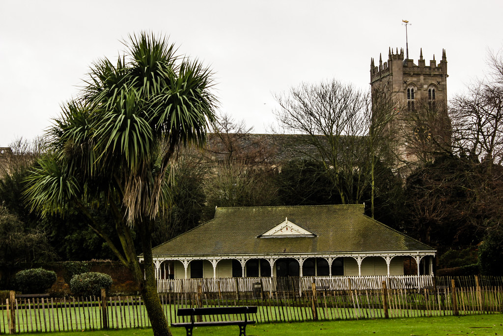 Priorato de Christchurch visto detrás de una cabaña y una palmera en un parque.