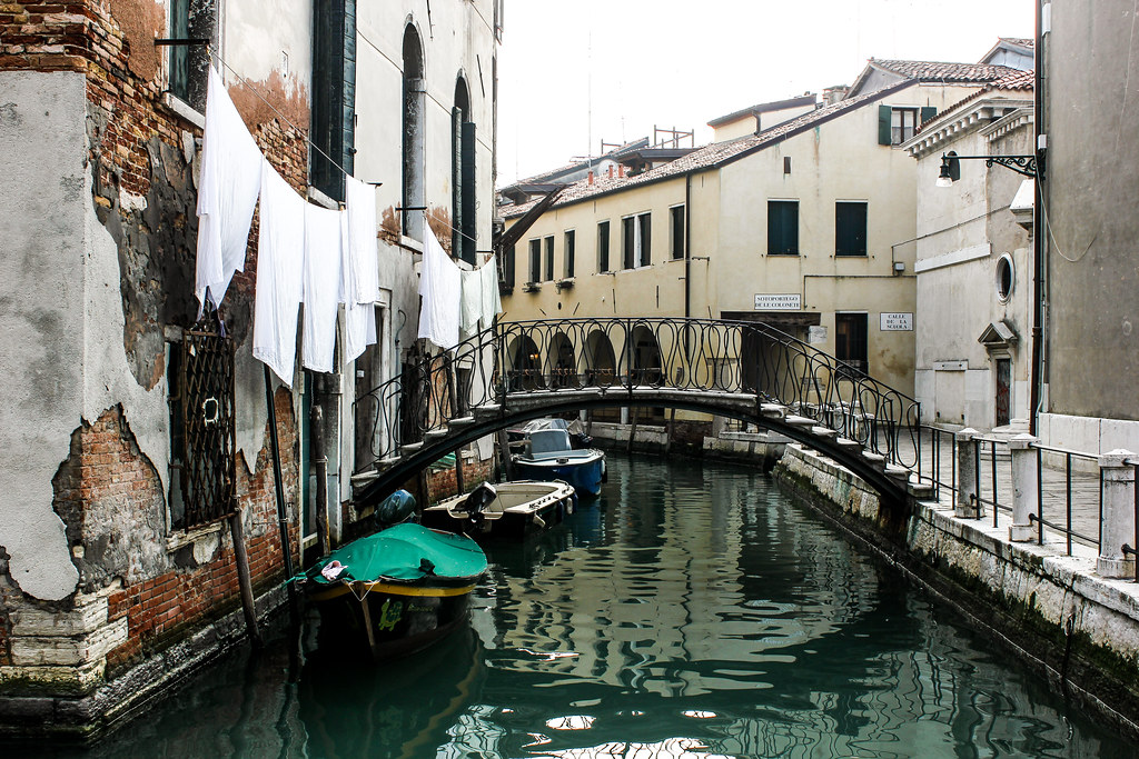Puente peatonal sobre un estrecho canal veneciano con ropa tendida.