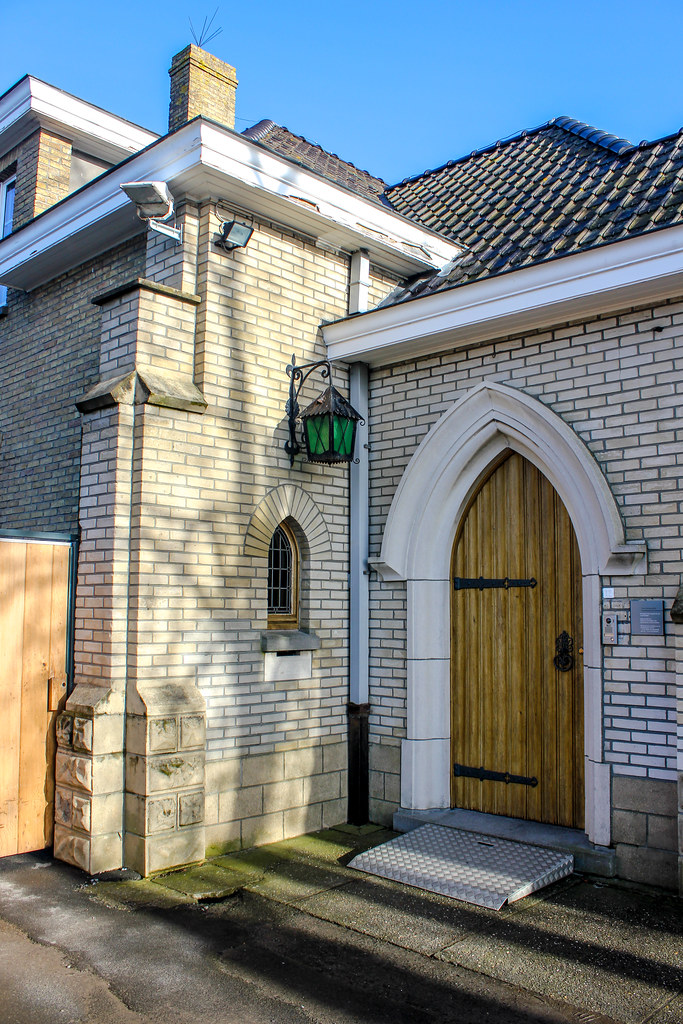 Puerta de entrada de madera en la fachada de ladrillo de la Abadía de Westvleteren en un día soleado.