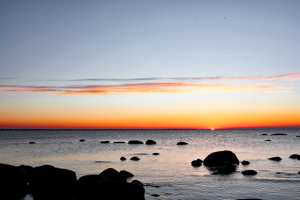Puesta de sol en la playa de Pärispea con cielo anaranjado y rocas en el Mar Báltico.