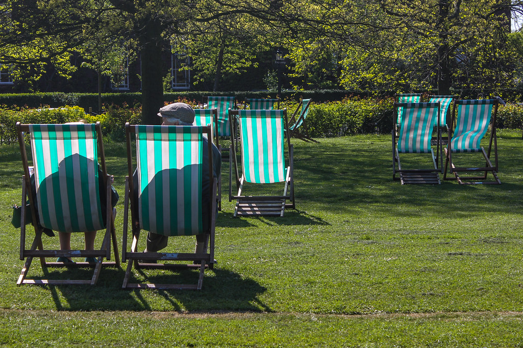 Pareja relajándose en sillas de playa a rayas verdes y blancas en Regent's Park, Londres, en un día soleado.