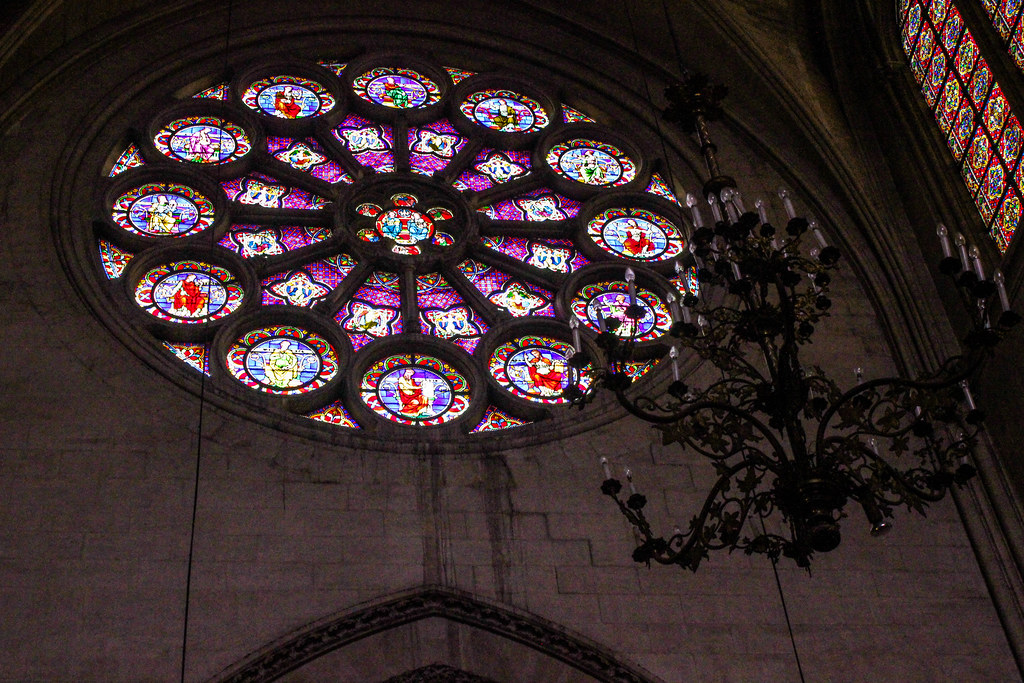 Rosetón colorido iluminado con luz natural en la Catedral de Saint-Pierre de Montpellier junto a un candelabro antiguo.