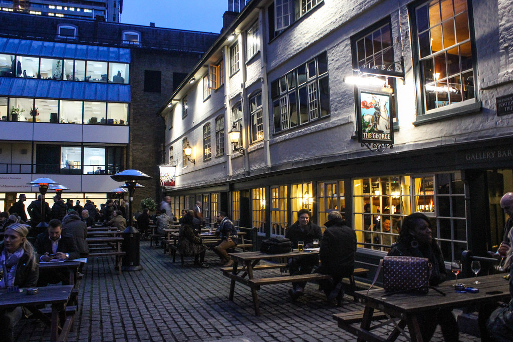 Patio del histórico The George Inn en Londres al anochecer con gente socializando.