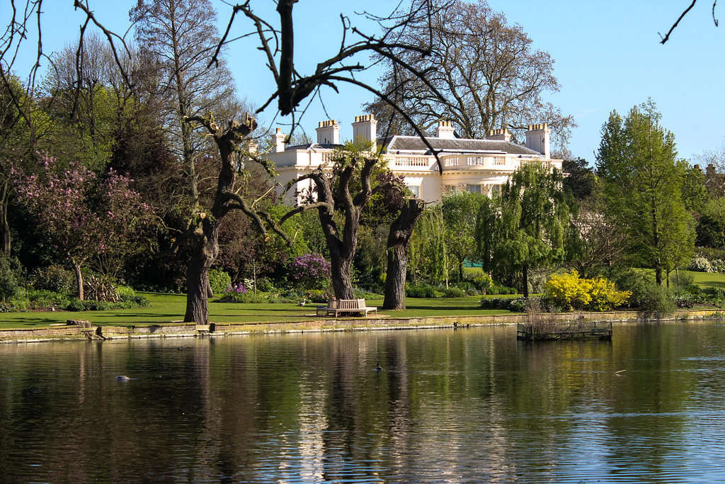 La propiedad The Holme reflejada en el lago de Regent's Park, rodeada de árboles en flor en primavera.