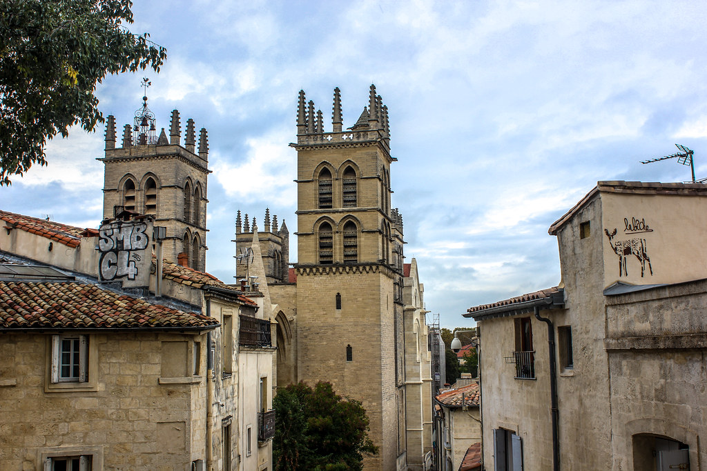 Torres de la catedral de Montpellier vistas desde entre los edificios con arte callejero en primer plano.