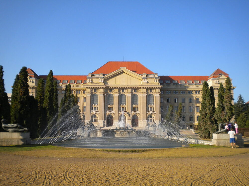 Fuente frente al edificio principal de la Universidad de Debrecen en un día soleado.
