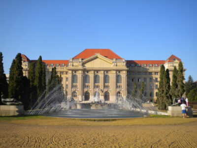 Fuente frente al edificio principal de la Universidad de Debrecen en un día soleado.