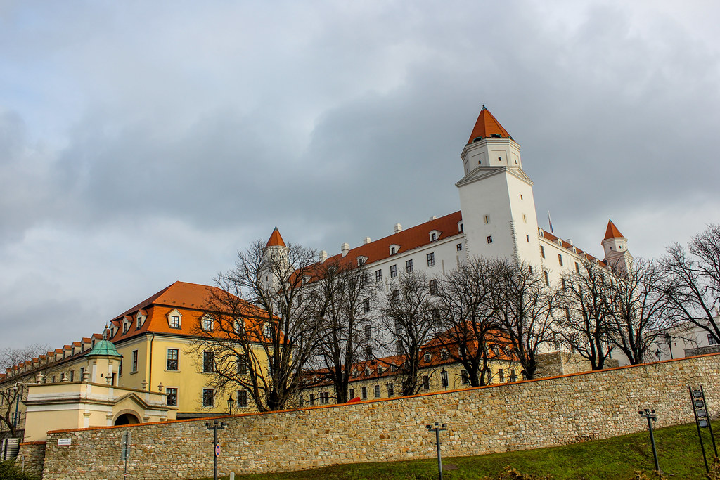 Vista del Castillo de Bratislava con sus torres blancas y tejados rojos bajo un cielo nublado.
