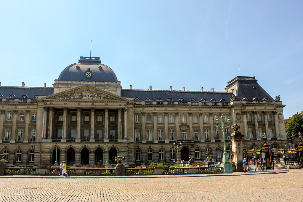 Vista frontal del Palacio Real con verja dorada y turistas en Bruselas, Bélgica.