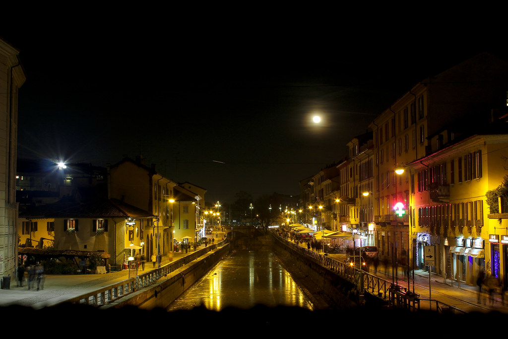 Vista nocturna del Naviglio Grande en Milán con luz de luna y restaurantes iluminados a lo largo del canal.