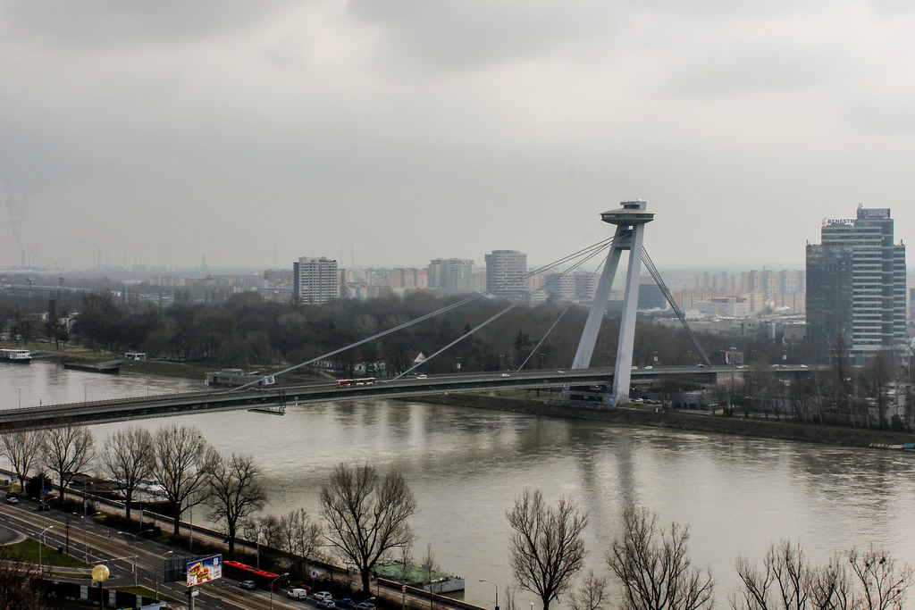 Vista panorámica del Puente Nuevo de Bratislava (Most SNP) que cruza el río Danubio en un día nublado, con edificios de la ciudad en el fondo.